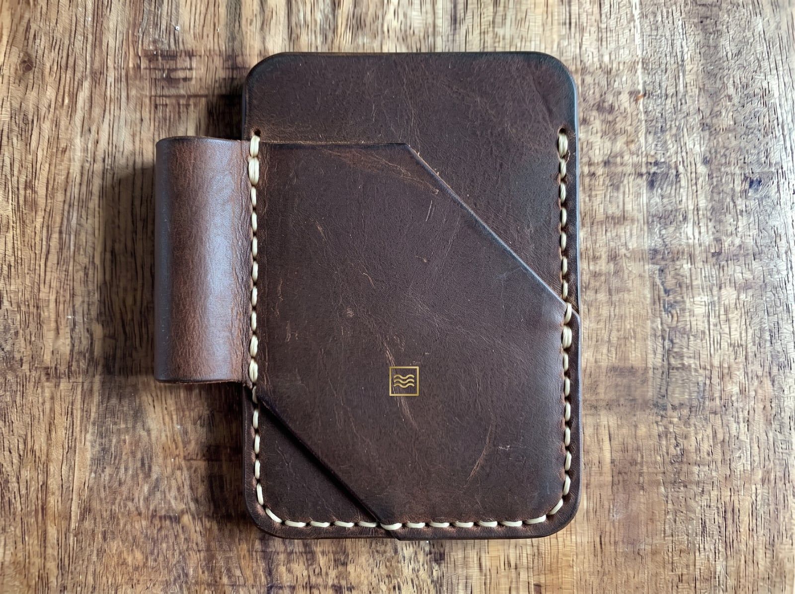 A card holder in dark crazy horse leather with an angled front pocket, a pen loop, cream saddle stitching and the Tidemark monogram in gold foil.