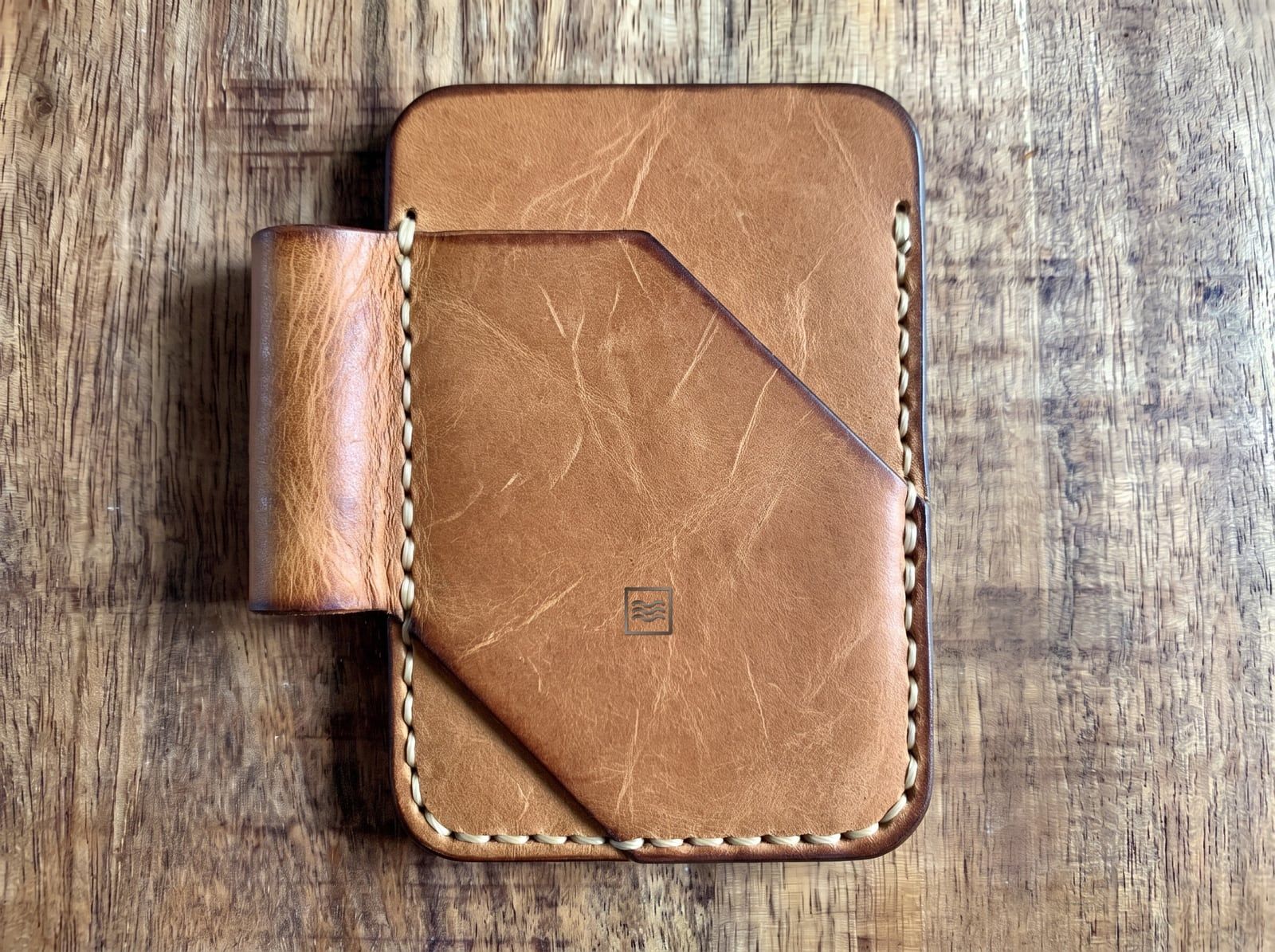 A card holder in light crazy horse leather with an angled front pocket, a pen loop, cream saddle stitching and the Tidemark monogram pressed blind into the leather.