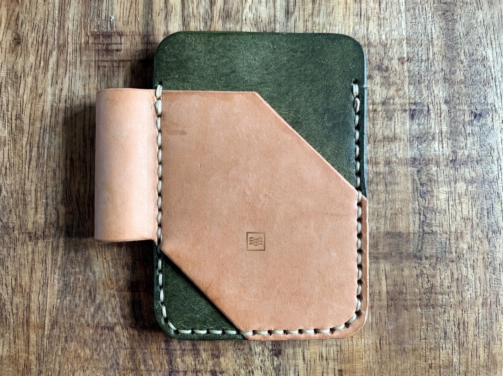 A card holder with an olive green back, a natural tan front pocket and pen loop, cream saddle stitching and the Tidemark monogram stamped on the pocket.