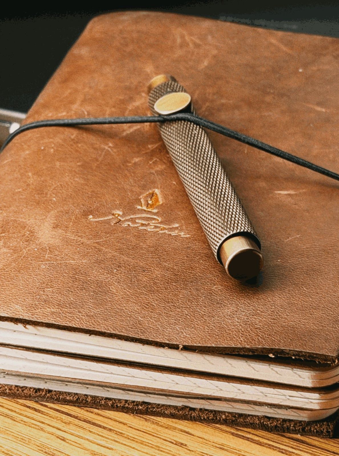Marek's leather notebook after ten years of daily use: worn, scratched leather, softened corners and the old mark on the cover, with a brass pen under the elastic. Not retouched.