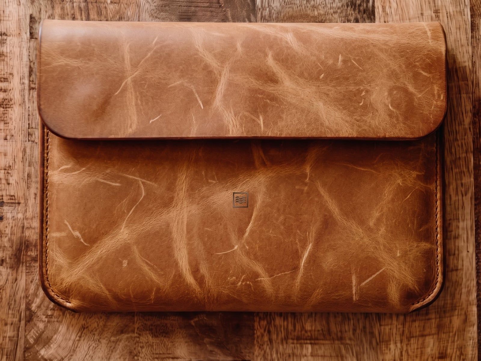 A closed sleeve in light crazy horse leather with a flap, stitched sides and the Tidemark monogram pressed blind into the leather.