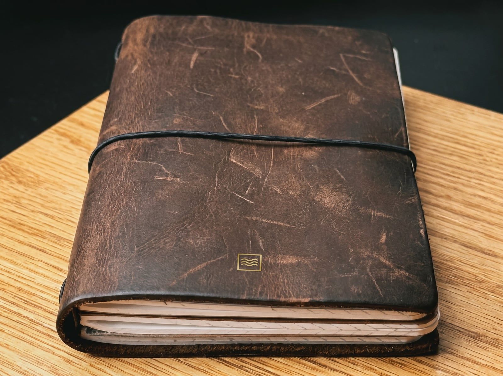 The System: an A6 cover in dark crazy horse leather with the Tidemark monogram in gold foil, an elastic cord and a stack of inserts.